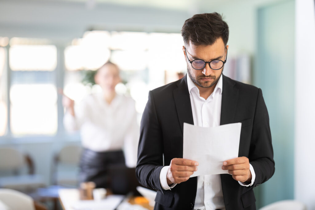 Sad man in suit and glasses standing in modern office, he holding resignation papers